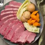 Sliced pressure cooker corned beef on plate with cabbage, potatoes and carrots