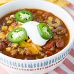 Taco soup in white bowl topped with sour cream and jalapeños.
