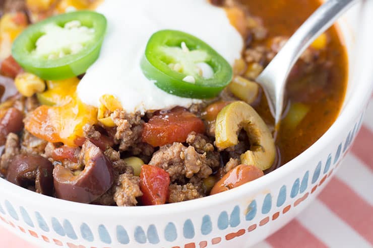 Taco soup in white bowl topped with sour cream and jalapeños.