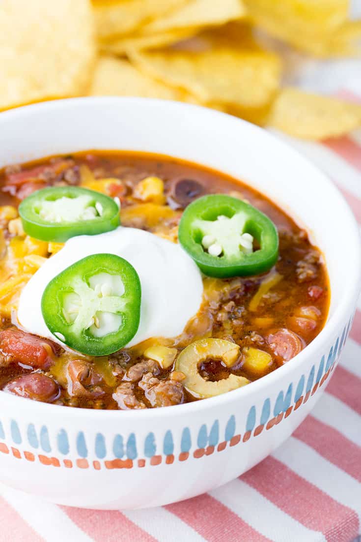 Taco soup in white bowl topped with sour cream and jalapeños.