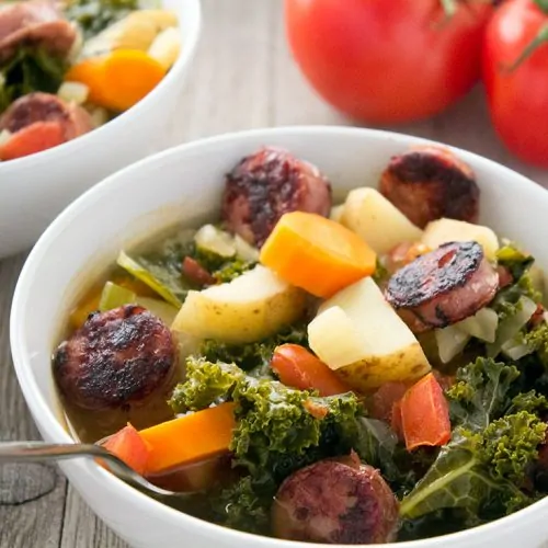 Sausage Potato Kale Soup in bowl with tomatoes in background.