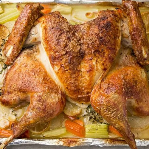 Spatchcock turkey on baking sheet with aromatics.