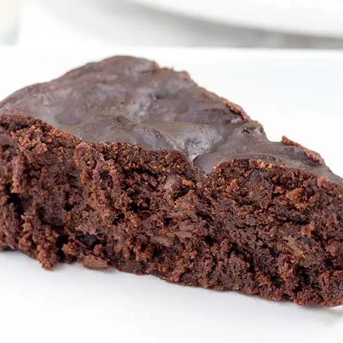 A slice of brownie on a white plate.