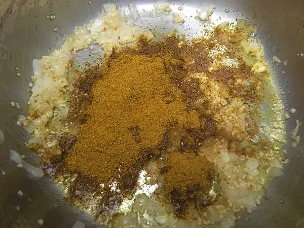 Aromatics sautéing in pot topped with curry powder.