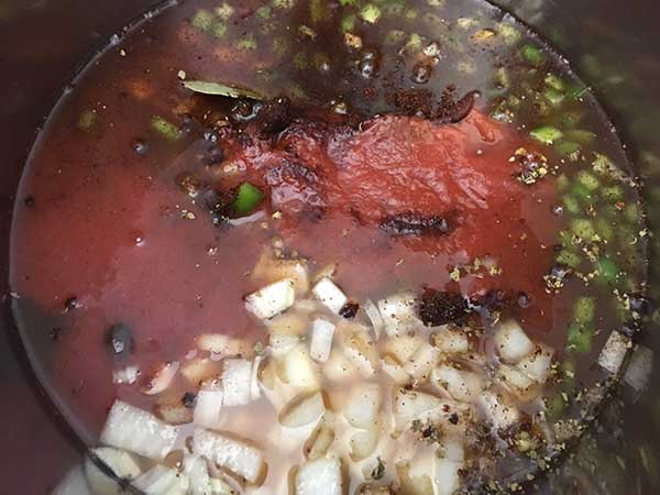 Beans, onions, green pepper and spices mixed with broth and tomato sauce in pot prior to cooking.