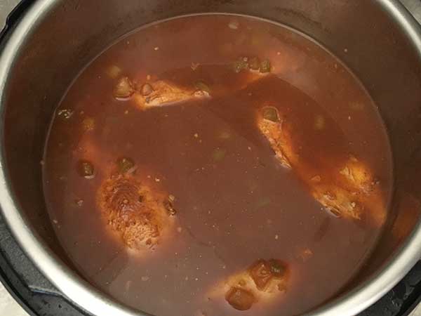 Cooked chicken breast submerged in chili tomato sauce liquid in Instant Pot.
