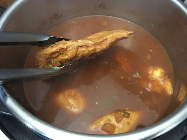 Cooked boneless chicken breast being removed from Instant Pot chili.