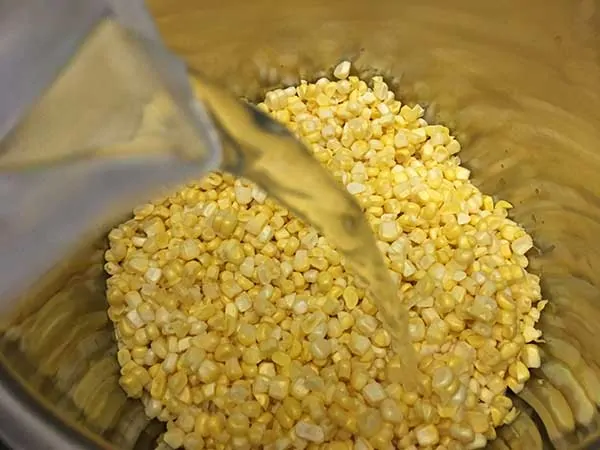 Poring water into pot with corn kernels.