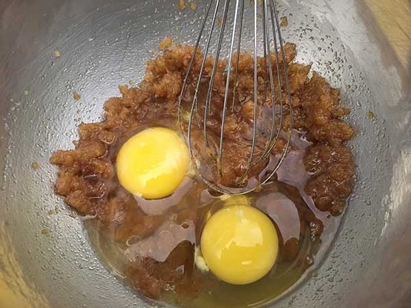 Eggs being whisked into brown sugar and butter mixture.