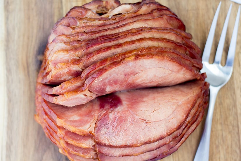 Overhead shot of spiral ham on wooden cutting board with serving fork.