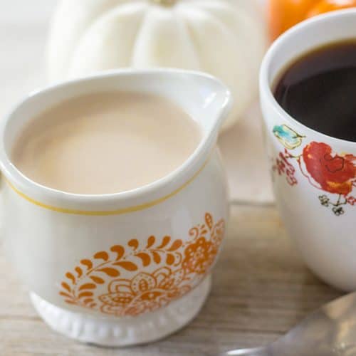 Pumpkin spice creamer in creamer dish, next to a cup of black coffee.