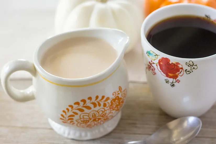 Pumpkin spice creamer in creamer dish, next to a cup of black coffee.