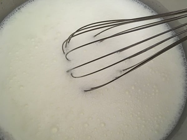 Milk and sugar being stirred with a whisk inside the Instant Pot inner pot.