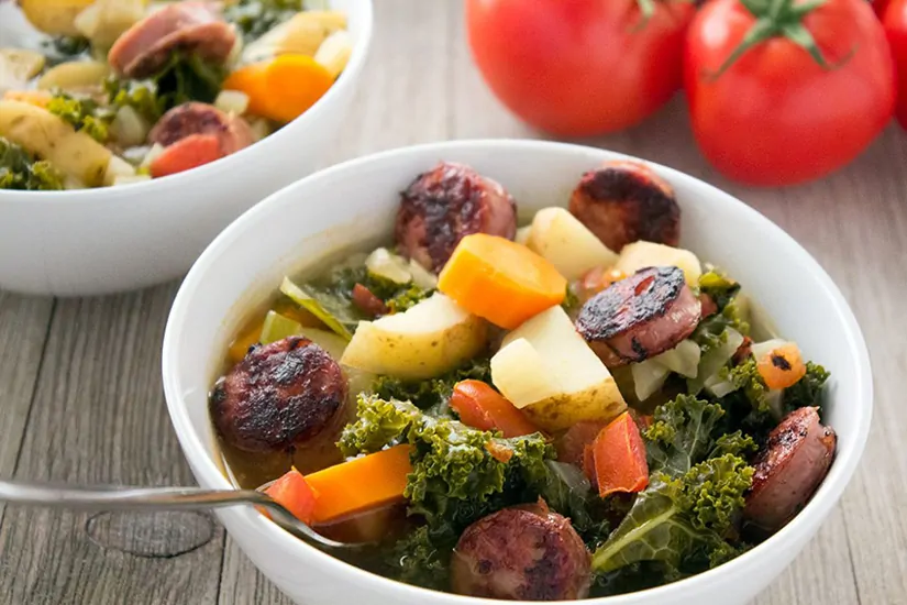 Sausage, Potato and Kale Soup in bowl with tomatoes in background