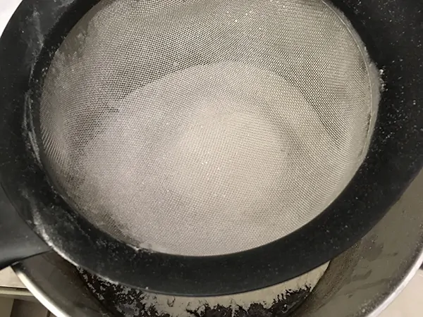 sifting flour with fine mesh strainer over pot