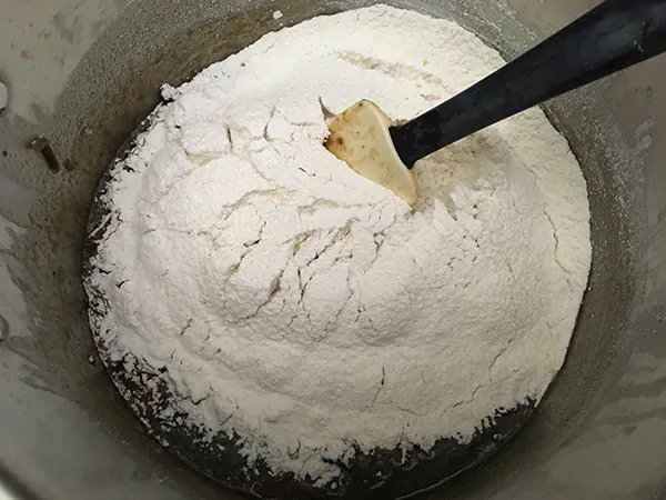 sifted flour on top of dried fruits in pot with rubber spatula