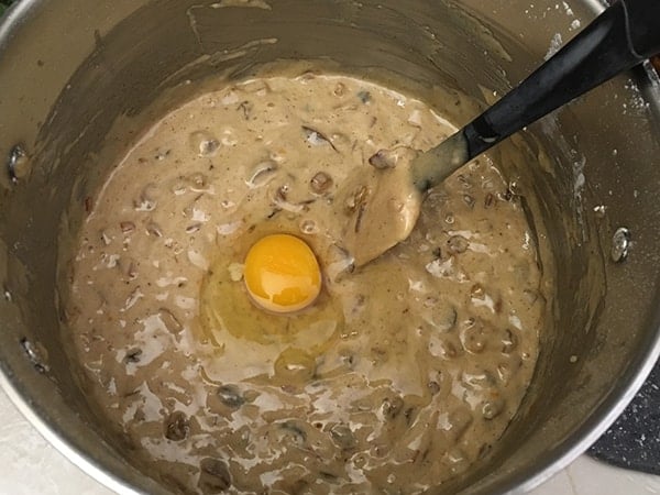 fruit cake batter with an egg in pot with rubber spatula