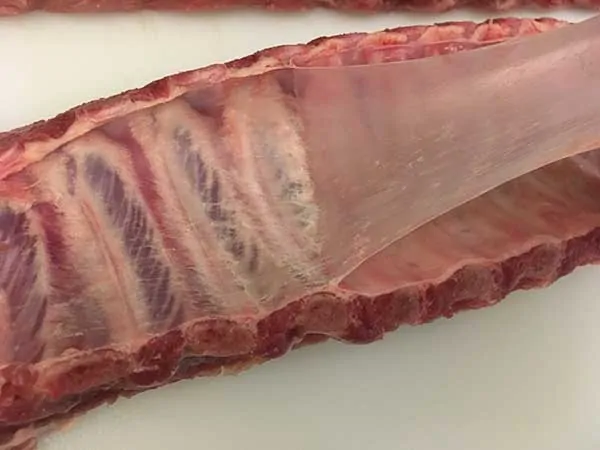 peeling membrane off ribs on white cutting board