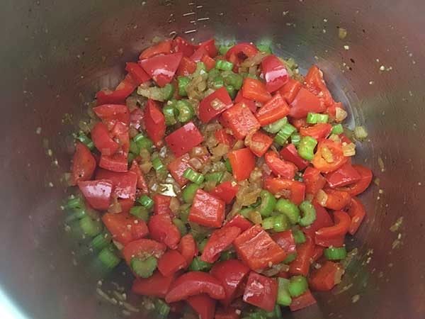 Sautéing diced onions, sliced celery, chopped red bell peppers, and minced garlic.