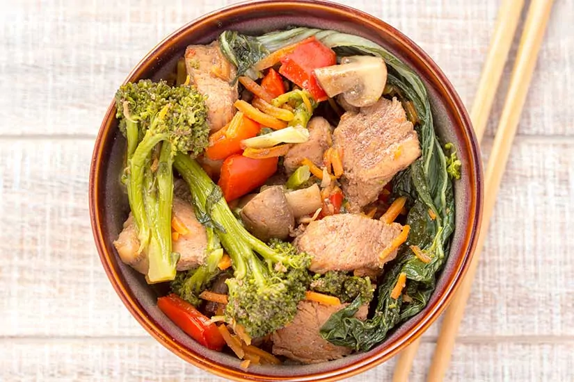 chicken stir fry in brown bowl with chopsticks.