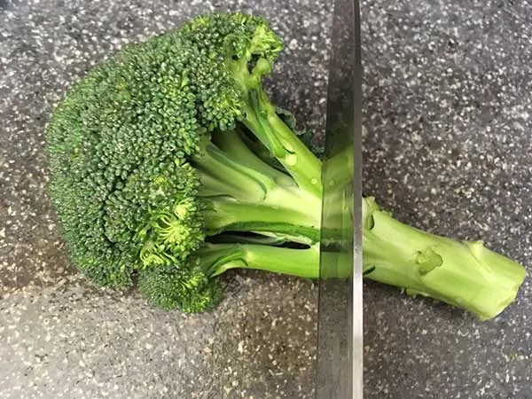 Head of broccoli on cutting board with knife.