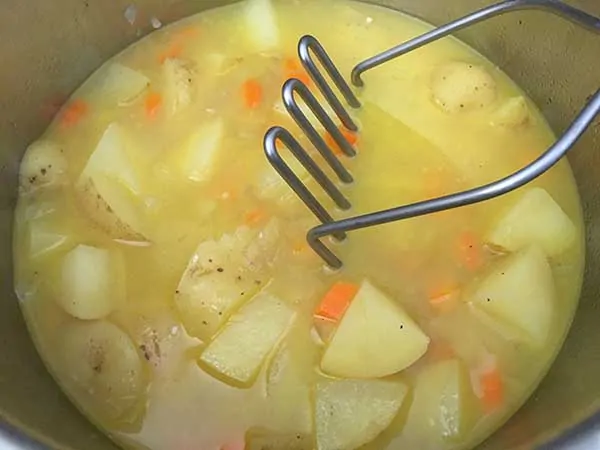 cooked potatoes in vegetable broth with potato masher