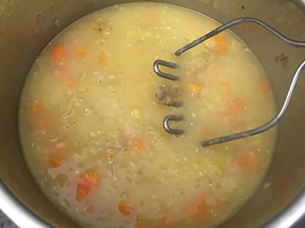 cooked potato soup with potato masher
