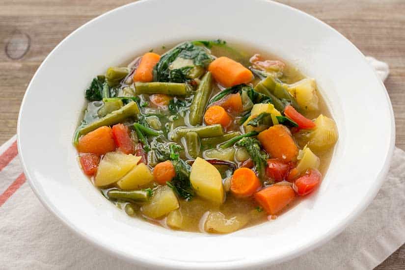 vegetable soup in white bowl with striped white linen on wood