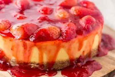 Strawberry-covered cheesecake on wood cutting board