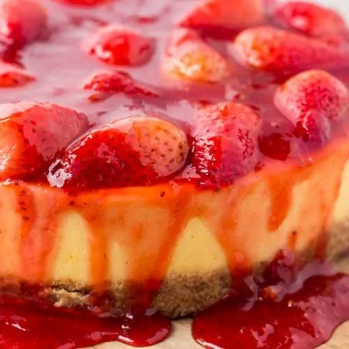 Strawberry-covered cheesecake on wood cutting board