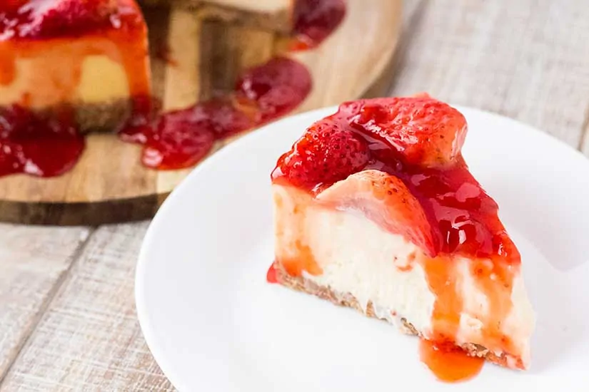 Slice of strawberry covered cheesecake on white plate.