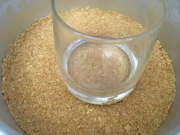 pressing graham crackers into an even layer for crust with a drinking glass