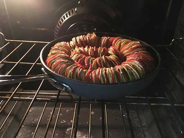 thinly sliced potatoes, tomatoes, zucchini, and squash in ratatouille pattern baking in oven
