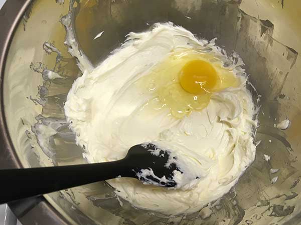 one egg on top of blended cream cheese and sugar in mixing bowl.