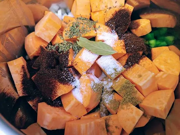 Spices and herbs on top of chopped sweet potatoes.