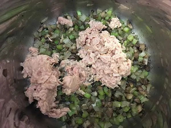 Two cans of tuna on to of sautéed veggies.