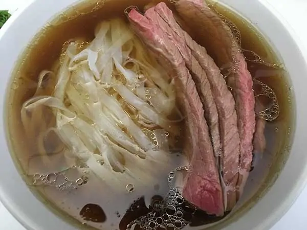 rice noodles, steak, and broth in bowl.