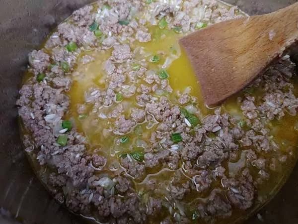 Meat mixture, rice, and broth combined with wooden spoon.