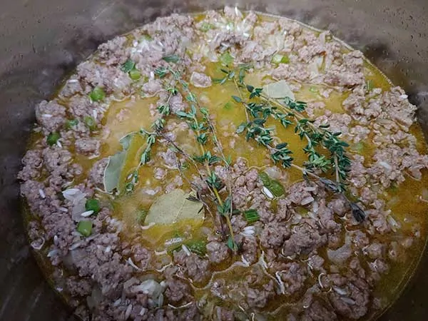Fresh thyme sprigs and bay leaves on top of meat mixture.