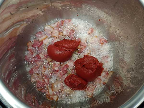 Tomato paste on top of bacon frying.