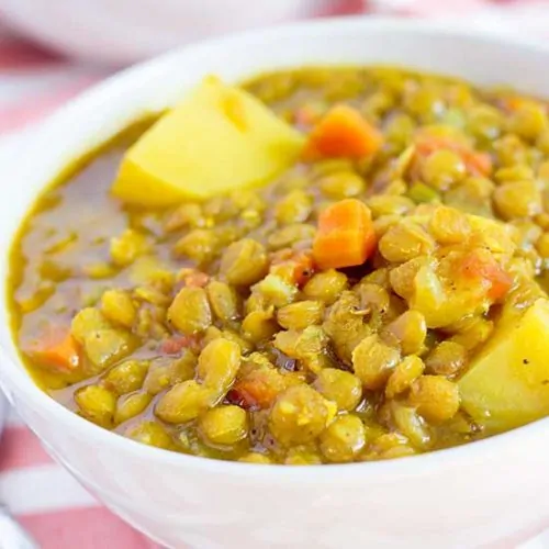 Lentil soup in white bowl with spoon and striped linen.