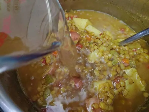 Pouring broth into lentil soup.