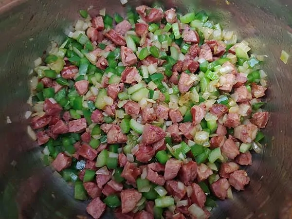 Crispy sausage cooking with diced onions, peppers, and celery.