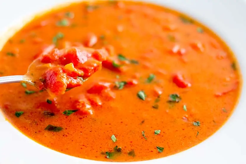 Tomato basil soup in white bowl with spoon.