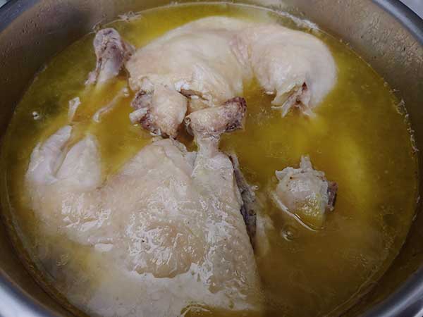Chicken leg quarters in broth in pot.