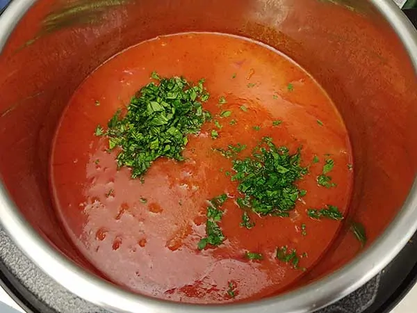 Finely chopped basil and parsley on top of soup in pot.