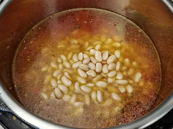 Vegetable broth in pot with aromatics and white beans.
