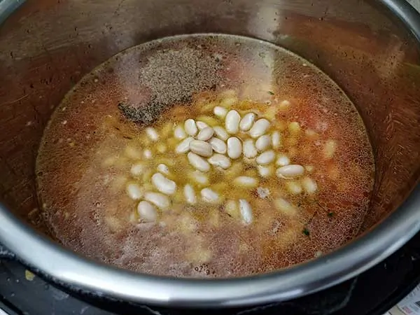 Vegetable broth in pot with aromatics, white beans, and pepper.