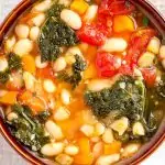 White bean soup in brown bowl with spoon in side.