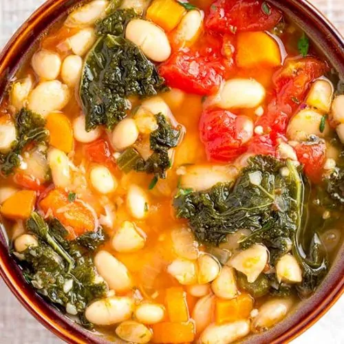 White bean soup in brown bowl with spoon in side.